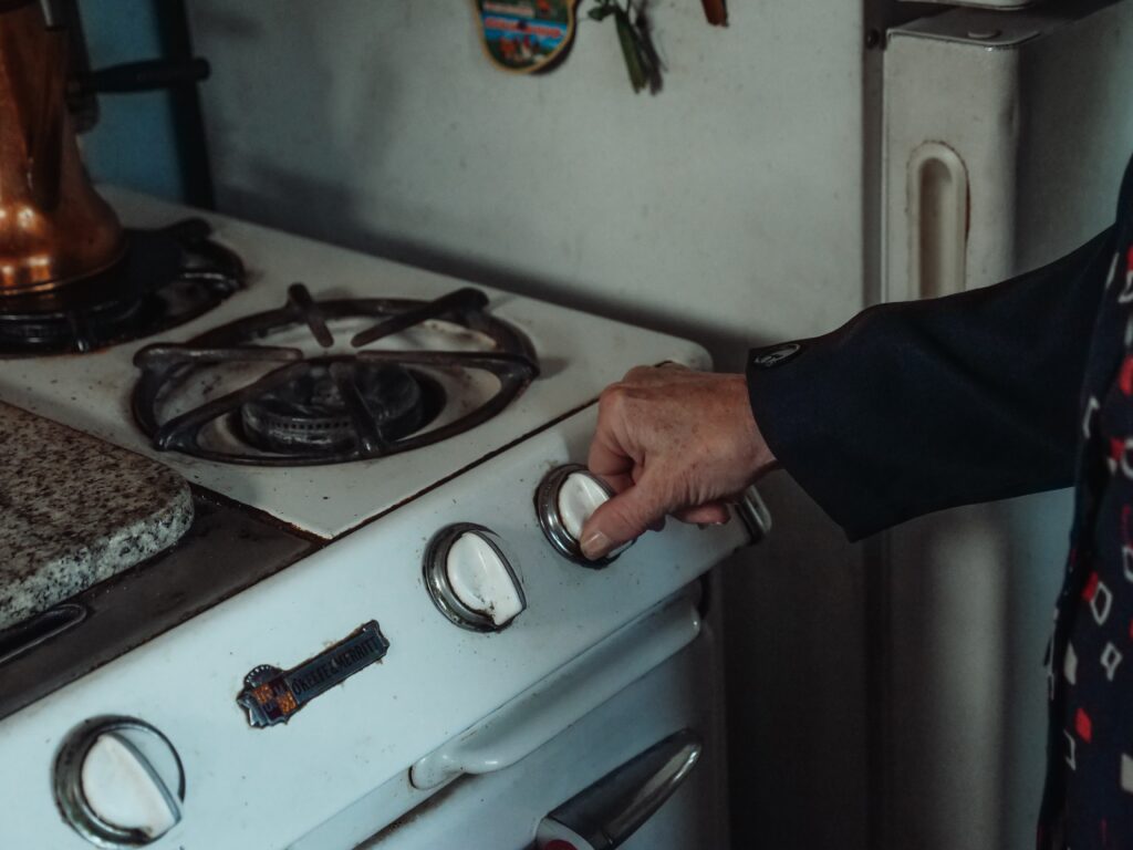 A person turning on a gas stove by turning the nob on the stove